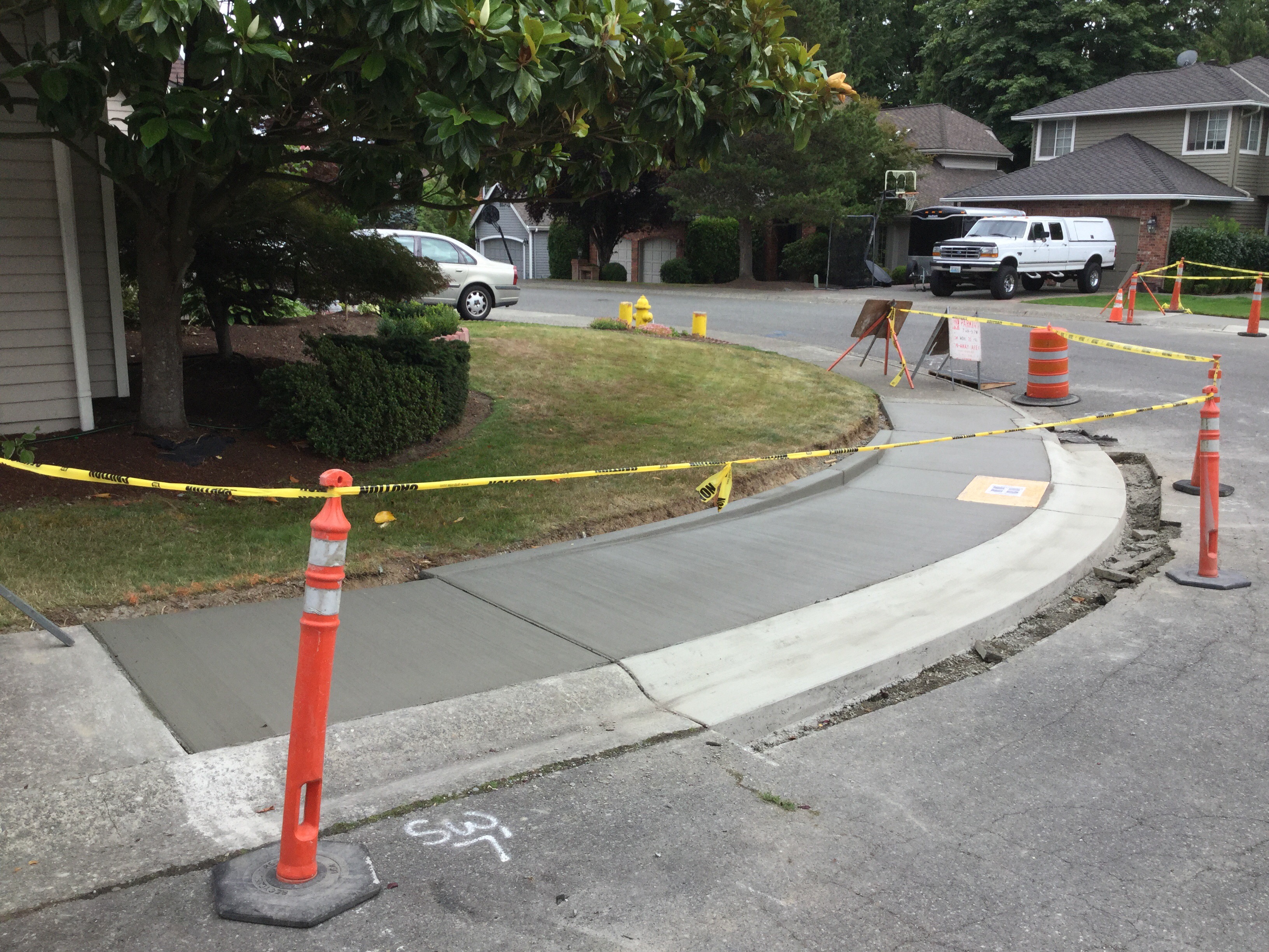 New pavement and accessible ramp at corner in residential area, protected by cones and tape