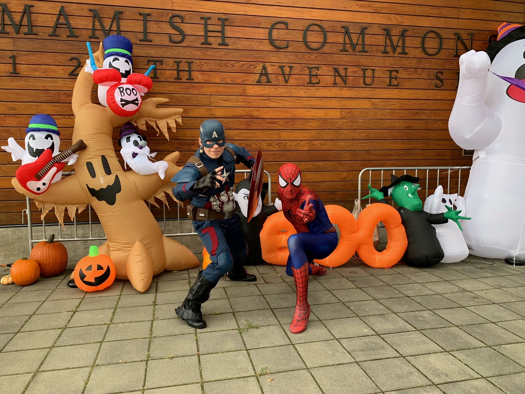 Two costumed character actors pose in front of the Sammamish Commons sign on the wall of City Hall. Inflatable Halloween decorations sit behind the actors.